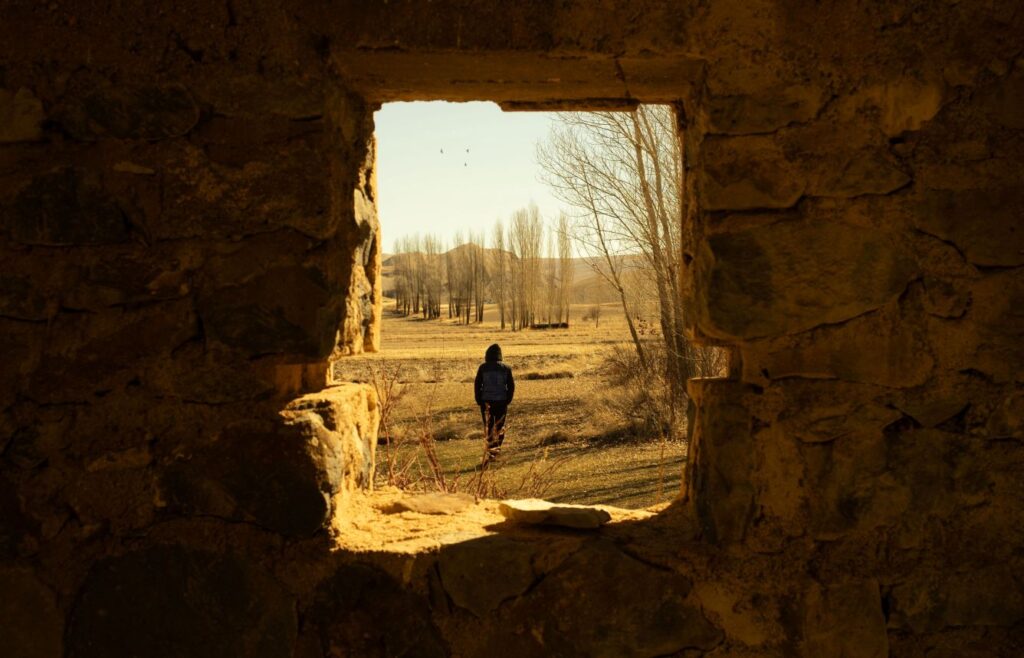 Person walking through a stone doorway toward a brighter future, symbolizing grit, perseverance, and the breakthrough that comes from not giving up.