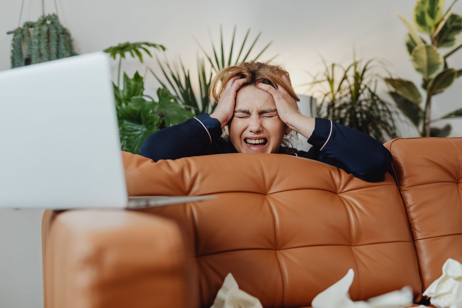 An overwhelmed woman clutching her head in frustration behind a laptop, illustrating the breaking point where you need books for productivity to regain control.
