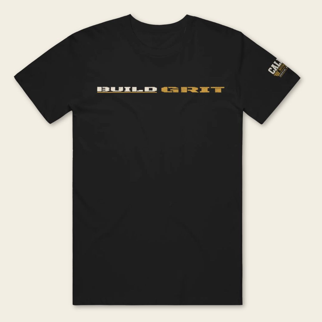 Front view of the BUILD GRIT Premium T-Shirt in Graphite Black featuring distressed BUILD GRIT artwork and a Caliber Motivation Co. sleeve patch.