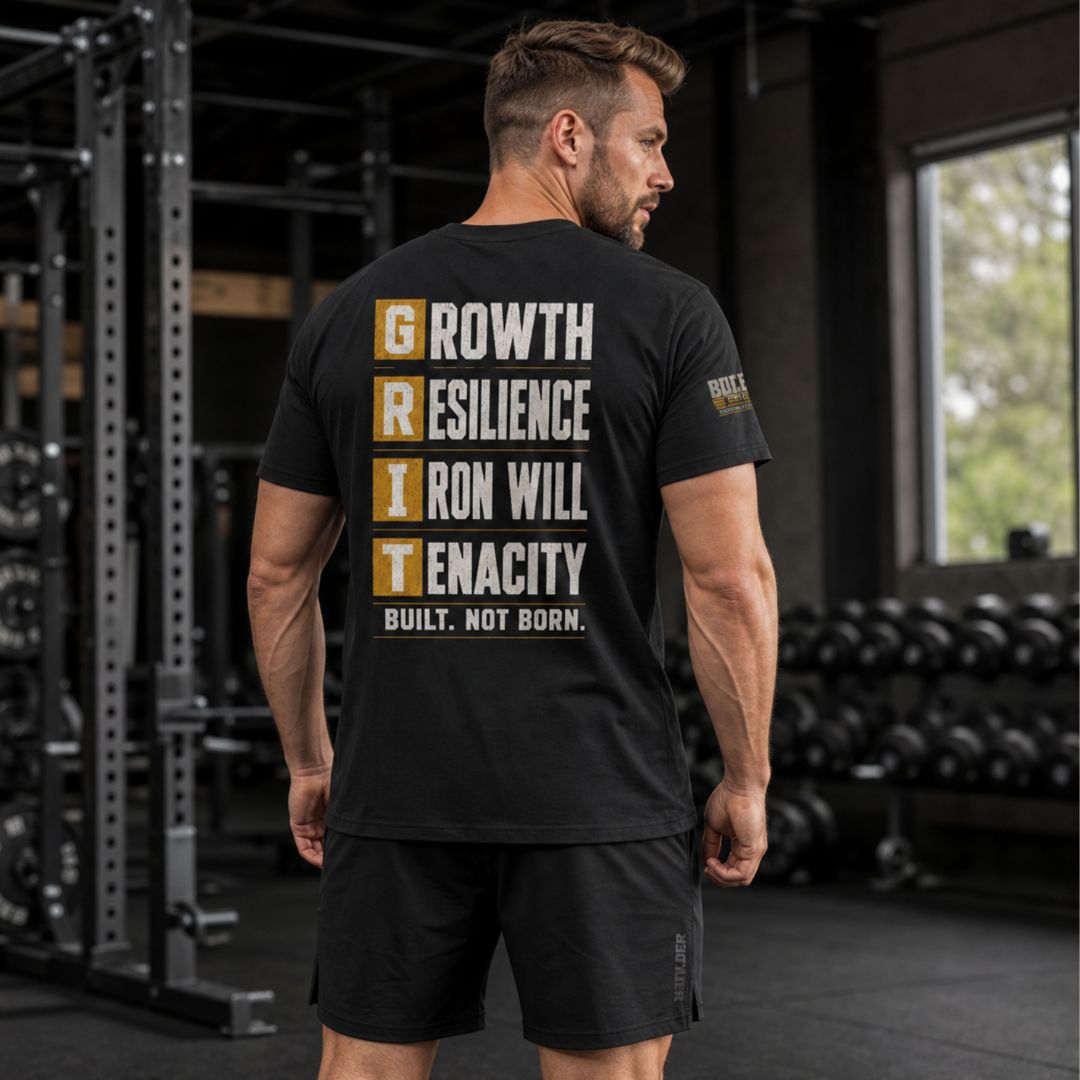 Back view of a man wearing the BUILD GRIT Premium T-Shirt in Graphite Black featuring the GRIT acronym design and Caliber Motivation Co. sleeve patch.