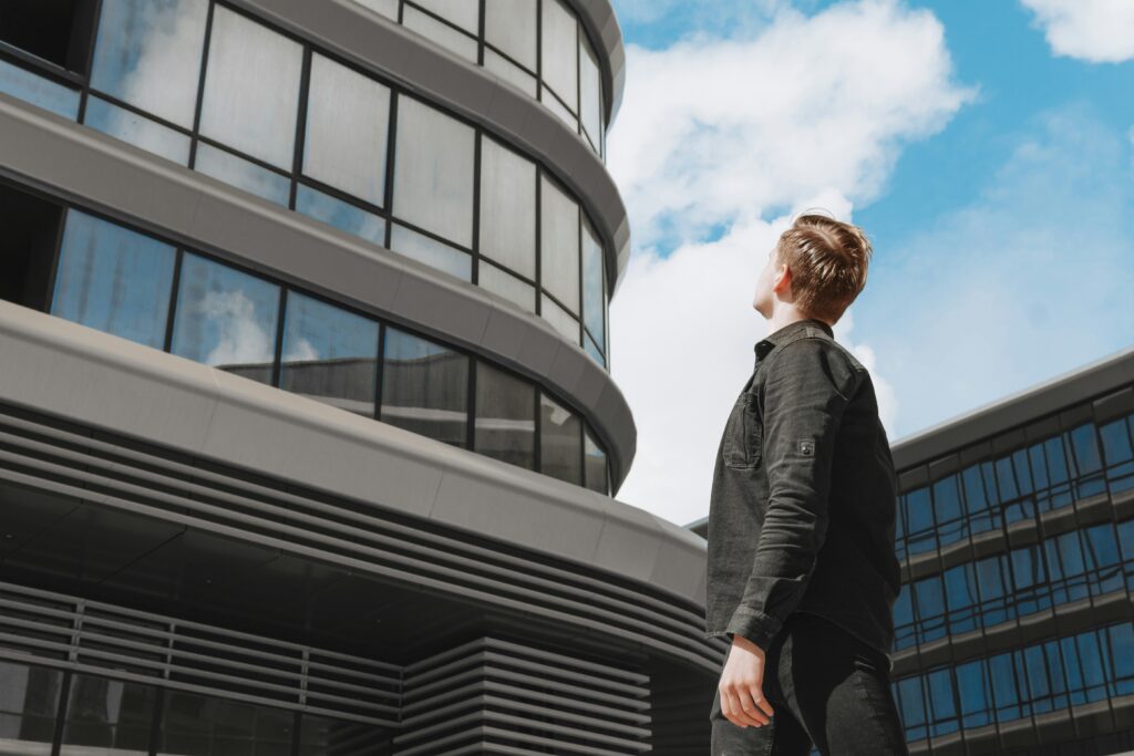 Person looking up at a modern office building representing how to overcome imposter syndrome without waiting for confidence.