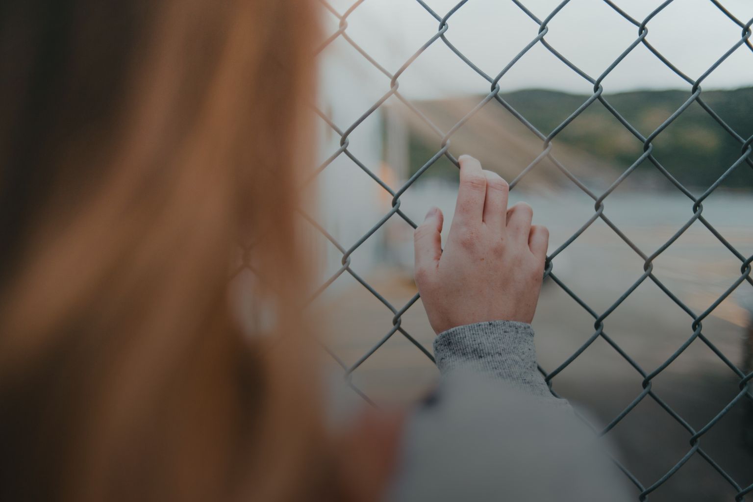 Person reaching toward a chain-link fence symbolizing the mental barriers behind saying I Can’t.