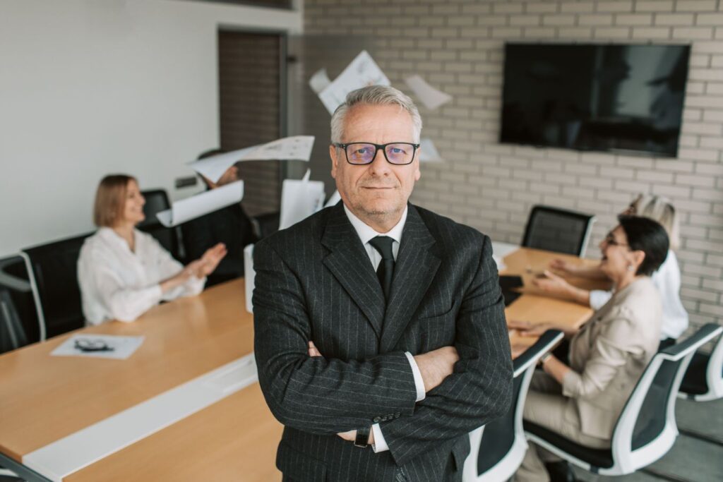 Calm business leader standing composed while workplace chaos unfolds behind him, illustrating how to be unbothered and master your reactions.