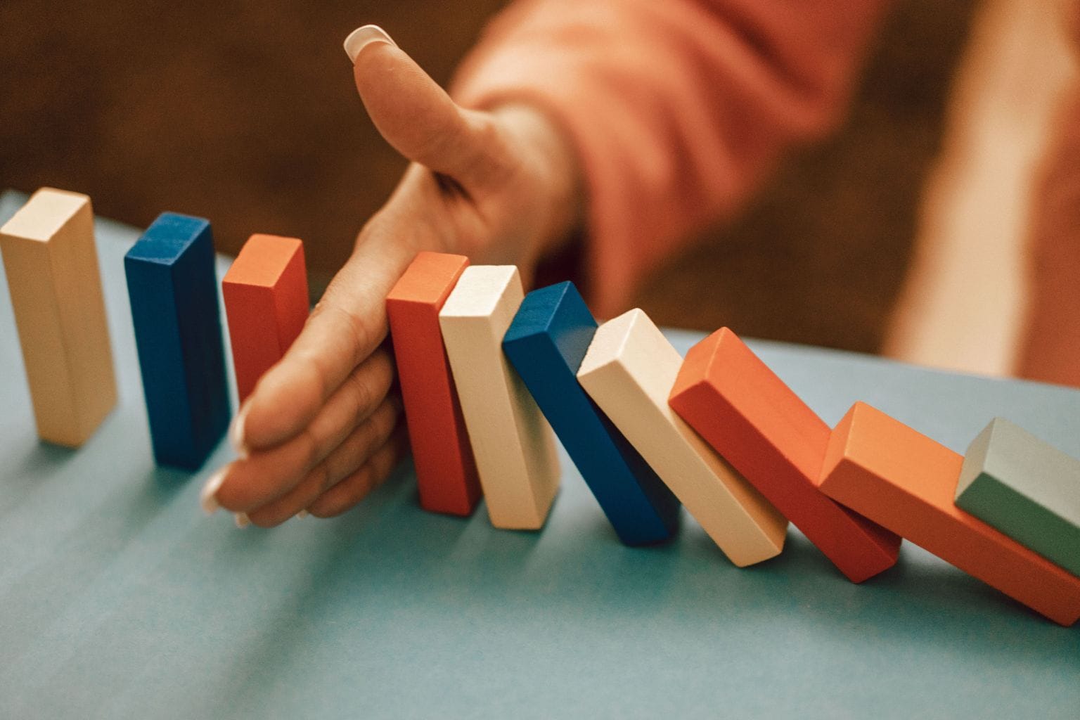 Hand stopping falling dominoes to represent Discipline Is Destiny and self-control