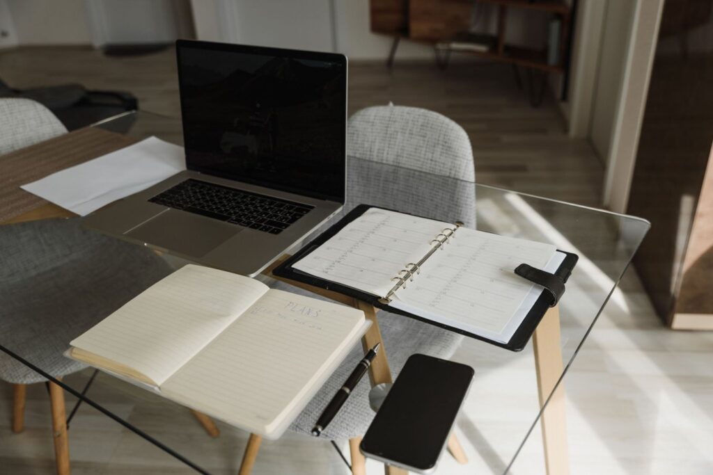 Simple home office setup with a laptop, planners, and smartphone for starting a virtual assistant business on a budget.