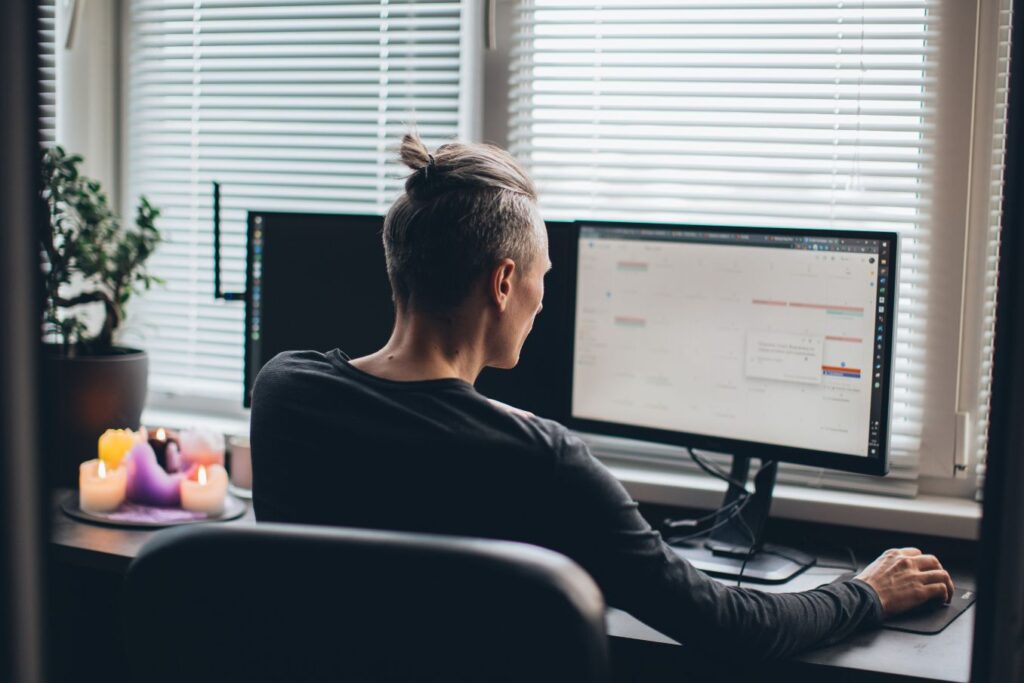 Man working at a home office computer with an online calendar open, preparing to manage clients for his virtual assistant business.