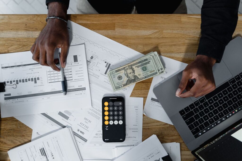 Business owner reviewing financial reports, cash, and calculator while planning recurring monthly income for a virtual assistant business.